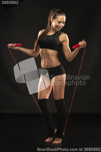Image of Muscular young woman athlete with a skipping rope on black 