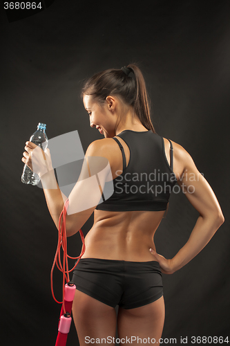 Image of Muscular young woman athlete with a skipping rope on black 