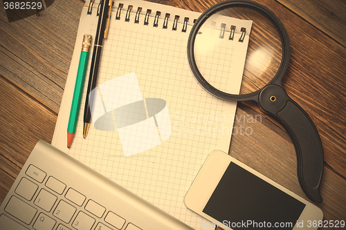 Image of notebook, computer keyboard, pen, pencil and magnifying glass