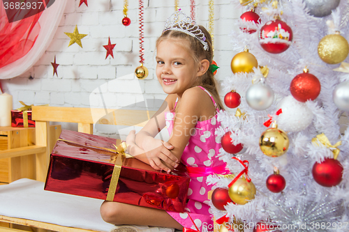 Image of Smiling girl sitting on a bench with a huge gift from the Christmas trees