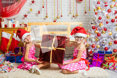 Image of Two funny girl holding a great gift sitting on a rug