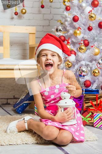Image of Girl screams happily holding candle in her hands and sitting by Christmas trees