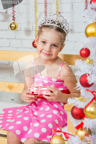 Image of Four-year girl sitting on a bench at a snowy Christmas trees