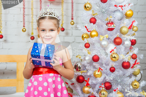 Image of Happy little girl holding a Christmas gift and standing near Christmas trees