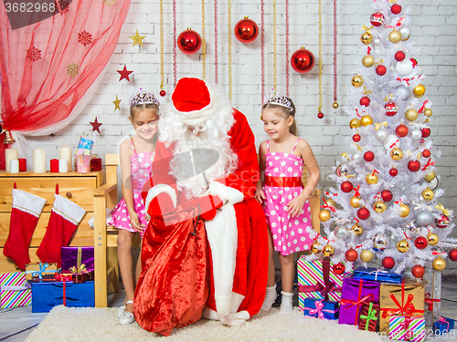 Image of Santa Claus pulls out a bag of gifts to two girls