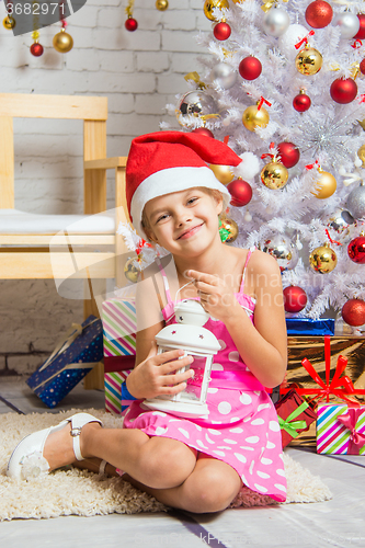 Image of Happy girl holding a candle in his hand and sitting at the Christmas trees