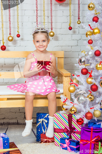 Image of Girl sitting on a bench with a gift in his hand a snowy Christmas trees