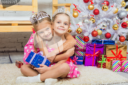 Image of Girl hugging another girl sitting on a mat at the Christmas tree