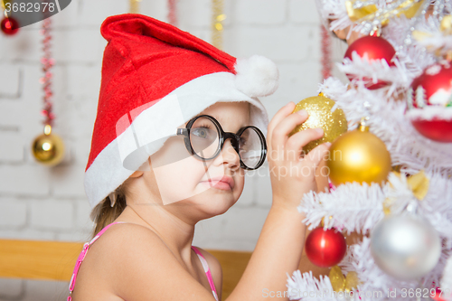 Image of Girl with round glasses hangs balls on a snowy New Years Christmas tree