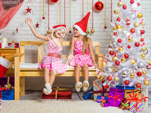 Image of Two funny girls fool around sitting on a bench in a Christmas setting