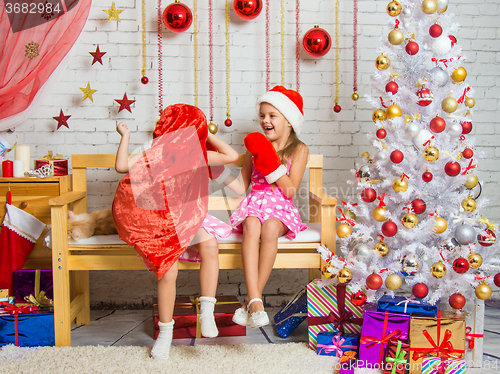 Image of Girl in a cap and mittens of Santa Claus laughing at the girl who put a sack on his head