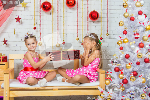 Image of Girl gives another girl a gift sitting on a bench in a Christmas setting