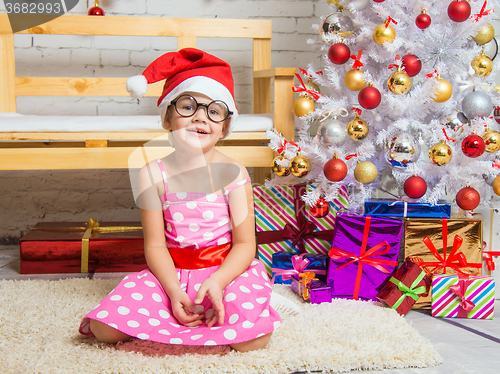 Image of Girl in the red hat and the funny round glasses on a rug in a Christmas setting