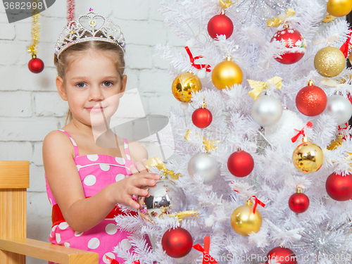 Image of Girl hangs balls on a snowy New Years Christmas tree