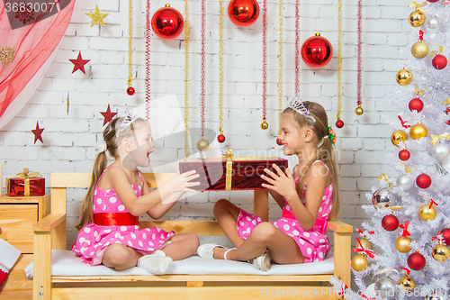 Image of Girls sitting on a bench in a Christmas atmosphere and keep the big red gift in hands