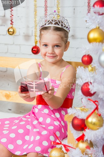 Image of Four-year girl stretches forward a little gift sitting snowy Christmas trees