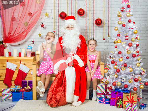 Image of Happy girls and Santa Claus sitting on a bench in a Christmas setting