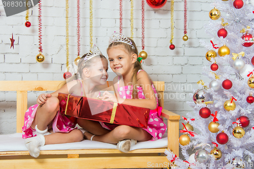 Image of Girl whispering a secret that some other girl sitting on a bench with a Christmas present