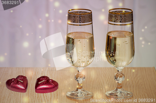 Image of Two wine glasses filled with champagne, and candles.