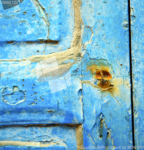 Image of dirty stripped paint in the blue wood door and rusty nail