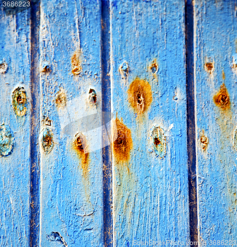 Image of dirty stripped paint in the blue wood door and rusty nail