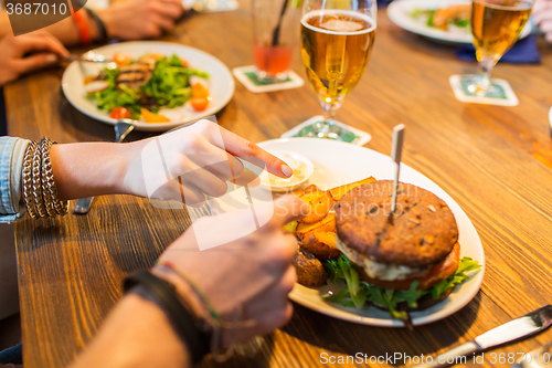 Image of close up of friends hands sharing burger at bar