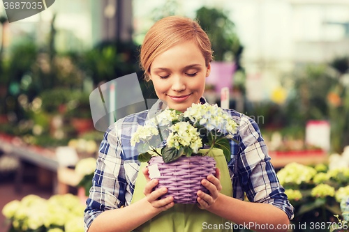 Image of happy woman smelling flowers in greenhouse