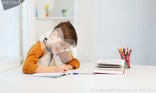 Image of smiling student boy writing to notebook at home