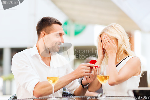 Image of happy couple with engagement ring and wine at cafe