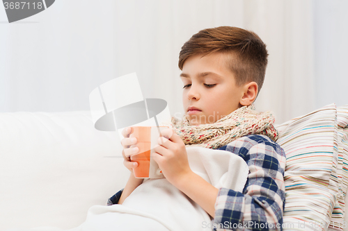 Image of ill boy with flu in scarf drinking tea at home