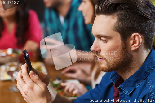 Image of man with smartphone and friends at restaurant