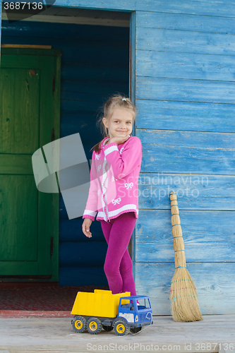 Image of Happy girl playing with the machine on the porch of a wooden house