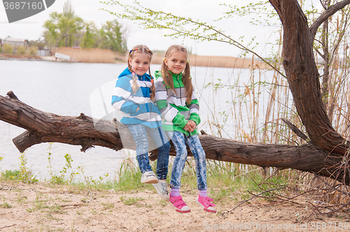 Image of Two girls sit on a fallen tree on the river bank