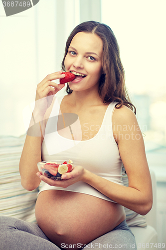 Image of happy pregnant woman eating fruits at home