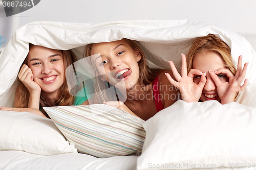 Image of happy young women in bed at home pajama party