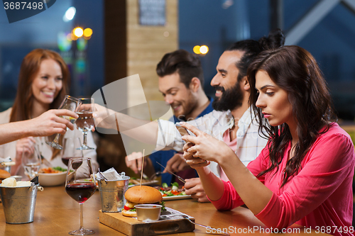 Image of woman with smartphone and friends at restaurant