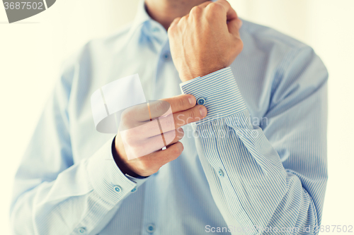 Image of close up of man fastening buttons on shirt sleeve