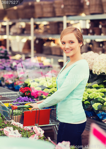 Image of happy woman with shopping trollye buying flowers