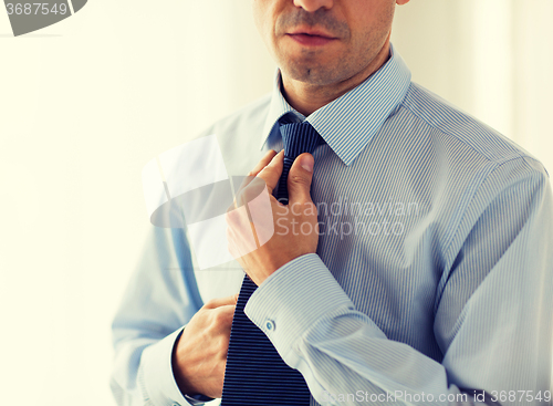 Image of close up of man in shirt adjusting tie on neck