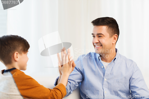 Image of happy father and son doing high five at home