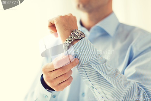 Image of close up of man fastening buttons on shirt sleeve