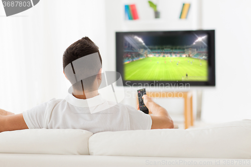 Image of man watching football game on tv at home from back