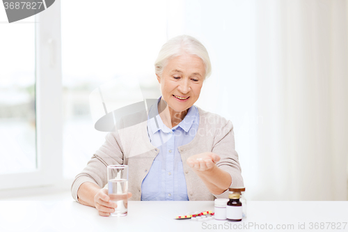 Image of happy senior woman with water and medicine at home