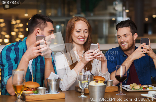 Image of happy friends with smartphones at restaurant