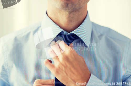 Image of close up of man in shirt adjusting tie on neck