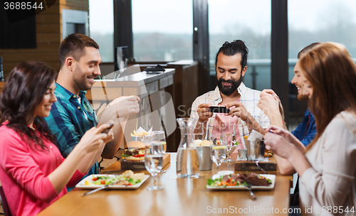 Image of happy friends taking picture of food at restaurant