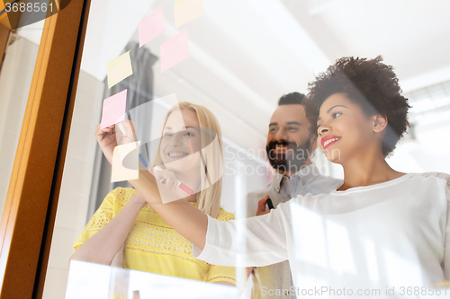 Image of happy creative team writing on stickers at office