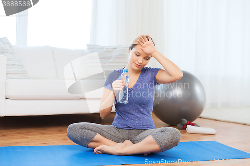 Image of tired woman drinking water after workout at home