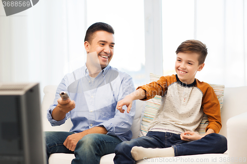 Image of smiling father and son watching tv at home