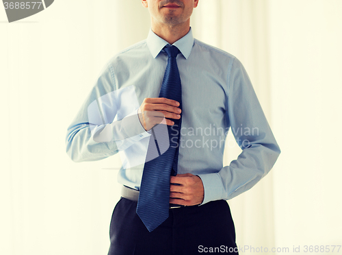 Image of close up of man in shirt adjusting tie on neck